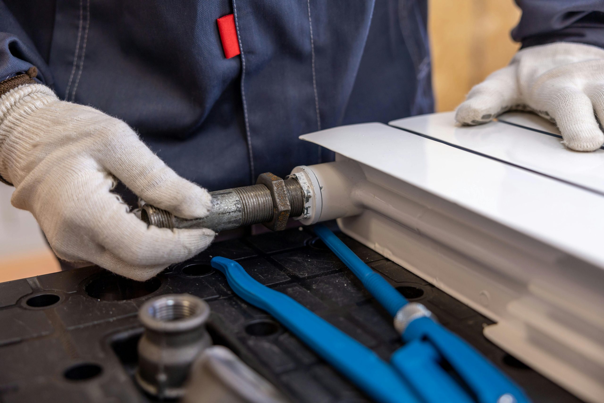 Technician installing metal pipe fitting on radiator unit with protective gloves
